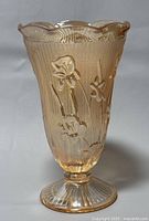 Front angled view showing the raised Iris floral pattern and scalloped edge with ribbed base of amber-colored Depression glass vase.