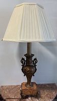 Full view of antique French spelter table lamp with marble base and pleated lampshade on a surface.