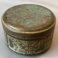 Top angled view of the circular bronze box showing patina and inscriptions on lid.