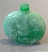 Front view showing detailed carving of traditional motifs on green jade bottle with stopper.