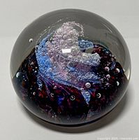 Front-side view of large glass paperweight showing intricate bubble swirls inside predominantly purple and blue.