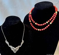 Two necklaces displayed on black velvet busts: one long coral bead necklace with gold-tone spacers, and one silver-tone rhinestone choker.