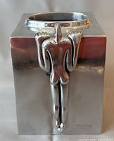 Front view showing sculpted human figure holding onto the edge of the tissue box cover and the polished silver-tone metal finish.