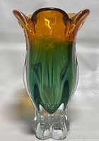 Front view of the multicolored heavy glass vase showing amber to green gradient with clear glass feet