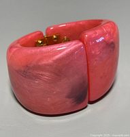 Chunky coral pink lucite bangle bracelet showing marbled darker accents and gold-tone hinge clasp visible