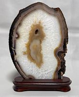 Frontal view of the polished natural agate slice on wooden base showing white crystalline interior and brown banding edges.