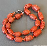 Coiled necklace on grey surface showing large coral barrel beads and silver-tone clasp.