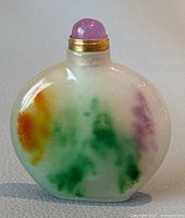 Front view of a natural jade flat bottle with multi-colored patches and rounded purple amethyst stopper with gold collar.