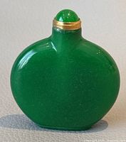Front view of natural green jade snuff bottle with gold band and rounded cap, showing smooth glossy surface and rich green color.