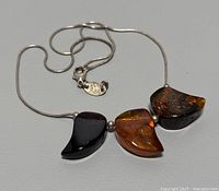 Photo showing the entire necklace laid flat with three amber stones and silver beads on the chain, highlighting the size and color of the stones.