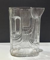 Front view of clear textured glass pitcher showing rectangular body, integrated handle on side and corner spout