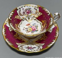 Top view of the teacup sitting inside the saucer showing the floral designs and gold detailing on magenta and white porcelain.