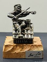 Front view of silver sculpture showing fiddler seated on rooftop, wood base with label