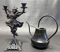 Photo showing both the metal watering can and one of the decorative lady dancing candle holders side by side on a dark background.