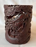 Front view of cylindrical vintage Chinese brush holder carved from bamboo, showing dragon and clouds in high relief, reddish-brown lacquer.