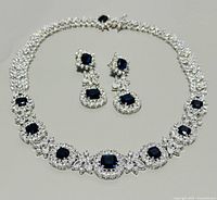 Full view of necklace and earrings set displayed flat, showing arrangement and design with blue stones and clear crystals