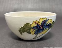 Side view of vintage Moorcroft bowl showing yellow and purple flower design with green leaves and crackle glaze.