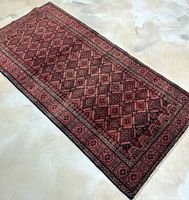 Full view of the vintage handwoven Persian Baluchi rug showing the red geometric diamond pattern and border.