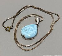 Overall view of the vintage natural larimar pendant necklace with the 20 inch silver chain laid out flat on a neutral surface.