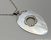 Close-up photo showing pendant detail with mother of pearl and silver accents.