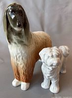 Two porcelain dog figurines on white background, one larger brownish and one smaller white dog