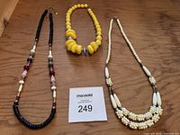 Three costume jewelry necklaces displayed on a wooden surface, showing overall appearance and colors.