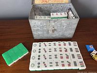 Metal case open showing Mahjong tiles laid out in front and inside the box