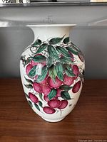 Front view of the porcelain vase showing rich pink lychee fruits and green foliage artwork on a white background.