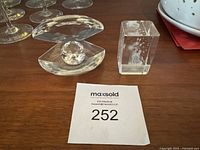 Two crystal glass figurines on wooden surface next to paper with lot number 252 visible.
