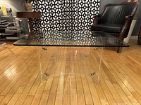 Full view of the mid century modern coffee table showing the clear rectangular glass top and curved Lucite legs with brass connectors.