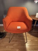 Front view of orange upholstered armchair with steel legs on wooden floor.