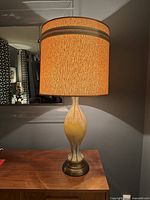 Mid century modern table lamp illuminated on wooden surface, showing height and shape.