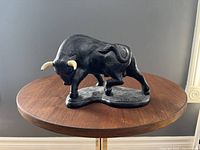 Front and side view of the black ceramic bull sculpture showing details of texture and cream-colored horns.