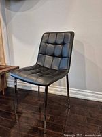 Front angled view of modern tufted vegan leather accent side chair showing upholstery and metal legs on dark wooden floor.