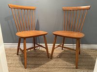Pair of vintage spindle back wooden chairs showing both chairs with natural wood finish, spindle backrests, contoured seats, angled legs with stretchers.
