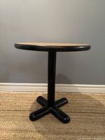 Side view of the round side table showing the black metal base and natural wood top.