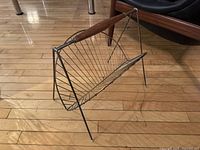 Side angled view of vintage brass magazine rack showing wireframe and walnut handle.