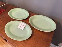 Three Fire King Jadeite green milk glass serving platters on wood surface: two ribbed rim platters and one smooth rim platter.