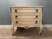 Front view of the vintage French Provincial dresser cabinet showing three drawers with brass ring pulls and curved front.