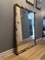 Rectangular vintage mirror standing upright against a wall, showing gold bamboo-style textured frame.