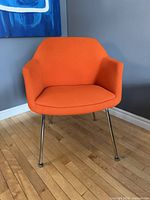 Front view of orange armchair showing curved back, integrated armrests, and seat cushion