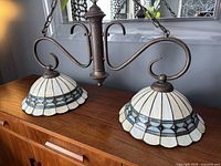 Photo showing the full double ceiling light fixture with two stained glass dome shades and ornate bronze metal arms on a wooden surface.