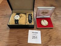 Watch box set showing wristwatch with white dial and green strap next to a black box inside with cushion, alongside vintage gold Fisker lighter in its box, labeled as lot 251.