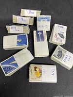 Overview photo showing ten stacks of vintage used US postage stamps with hand-labeled bands indicating 100 stamps each separated by lot numbers.