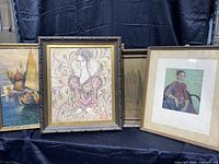 Four framed artworks arranged on black fabric including the Knitch La Mousme tapestry print, a ship scene painting, a Van Gogh print, and a painted portrait of a woman.