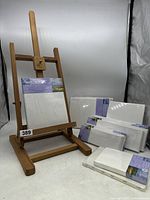 Wooden easel supporting one canvas panel with remaining canvas panels stacked beside it, showing original packaging
