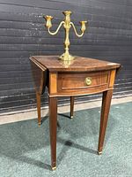 Front view of wooden drop leaf side table with brass candelabra on top.