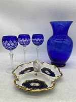 Three cobalt blue cut crystal wine glasses with clear faceted stems, a cobalt blue glass vase, and a divided fine China serving dish with floral and gold accents.