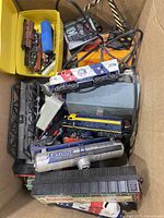 Full box view showing multiple model trains including the patriotic 1776 locomotive, blue Santa Fe locomotive, Bud Dry tank car, and some power supplies and parts.