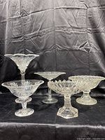Front view of five clear etched crystal compote candy dishes arranged against black backdrop